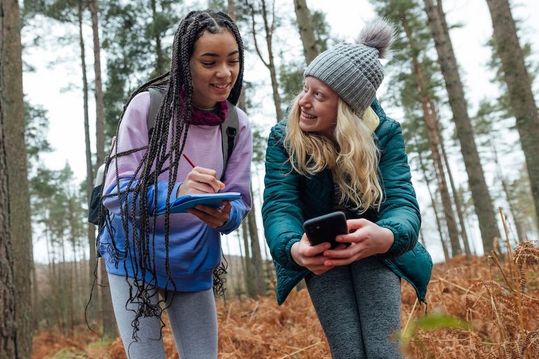 Zwei Mädchen sind mit dem Handy im Wald unterwegs.
