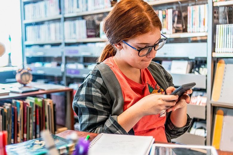 Ein Mädchen steht in der Bibliothek und konzentriert sich auf ihr Handy.