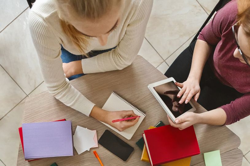 1178550125 Jugendliche sitzen gemeinsam an einem Tisch und machen Notizen.
