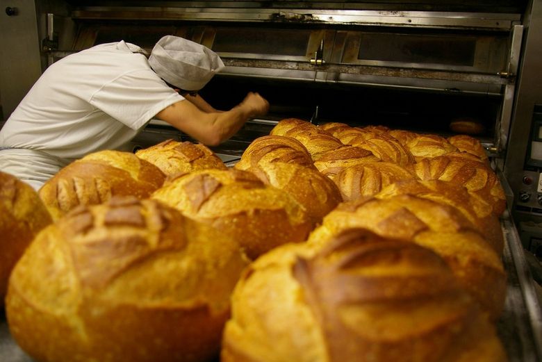 Ein Bäcker holt Brot aus dem Ofen.
