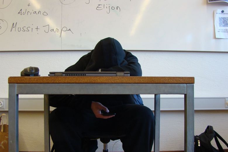 Ein Jugendlicher im Hoody legt seinen Kopf auf das Schulpult.