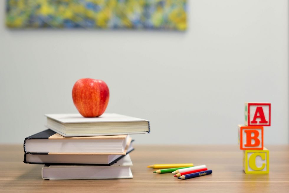 Schulbücher, Stifte, ein Apfel sowie Klötze mit Buchstaben, alles auf einem Pult angeordnet.