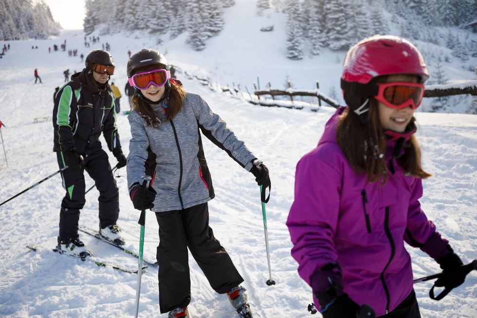 Kinder fahren lachend eine Skipiste hinunter.