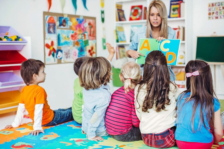 Eine Gruppe von Kindern sitzt auf dem Boden und hört einer Lehrerin zu, die das Alphabet erklärt. Foto: iStock/svedikd