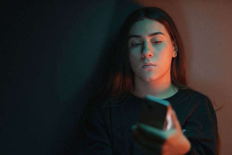 Ein Schatten fällt auf das Gesicht einer Teenagerin, die auf ihr Handy schaut.