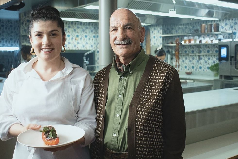 Eine Köchin steht in ihrer eigenen Restaurantküche, daneben ihr Vater.