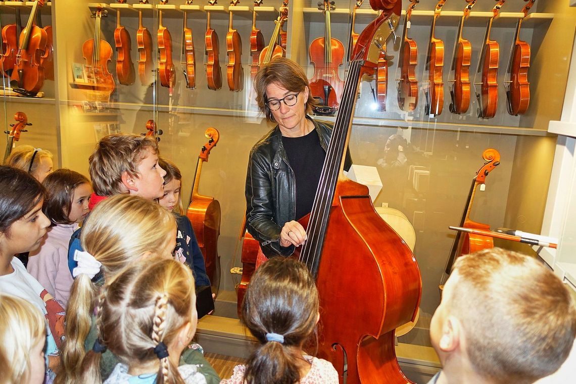 Eine Frau steht mit einem Kontrabass vor einer Kindergruppe.