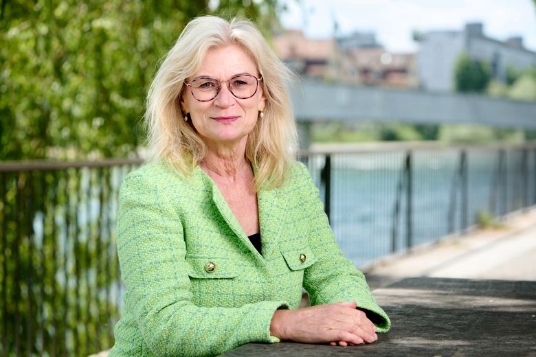 Frau mit grüner Jacke am Flussufer.