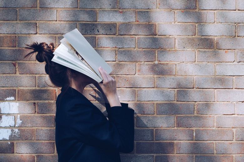 junge Frau hält sich ein geöffnetes Buch vor den Kopf.