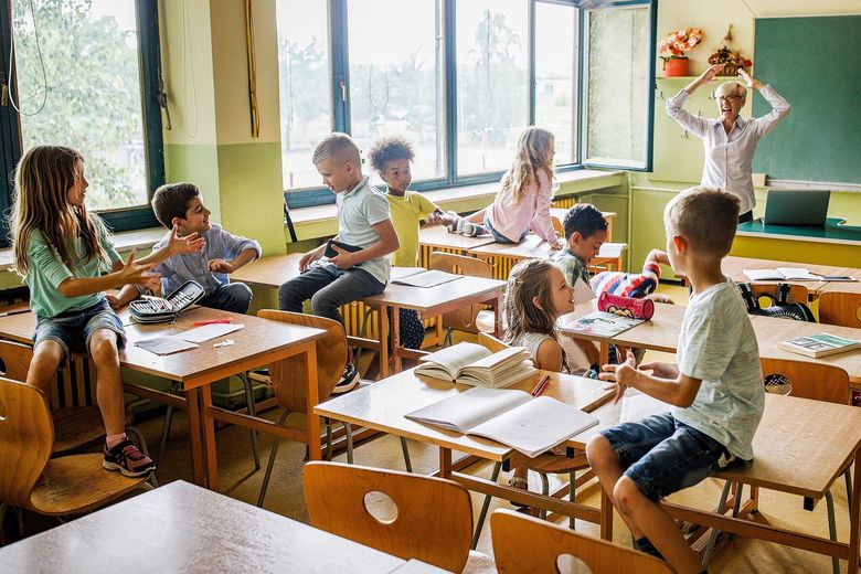 Schulkinder, die auf Pulten sitzen und schwatzen. Im Hintergrund eine überfordert die Hände über dem Kopf zusammenschlagende Lehrerin.
