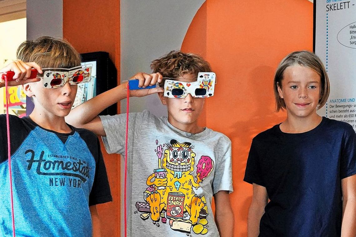 Drei Jungen stehen vor einer Wand. Zwei von ihnen haben je eine Brille mit einem Griff daran aufgesetzt.