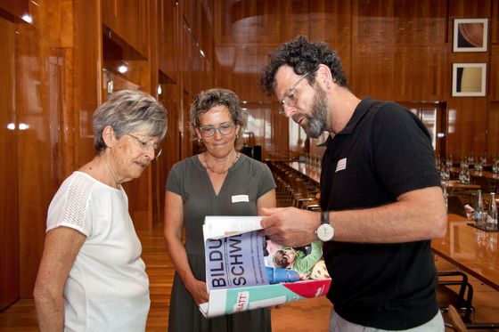 Zwei Frauen und ein Mann blättern durch das Magazin BILDUNG SCHWEIZ.