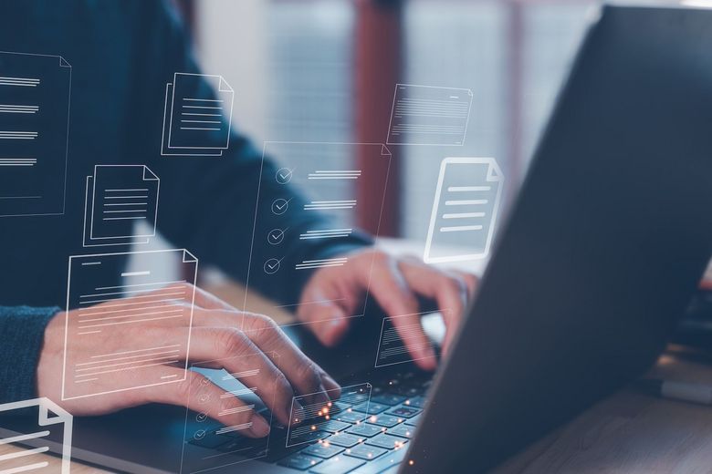 Ein Mann tippt in einen Laptop, der von Dokument-Zeichen umgeben ist. 