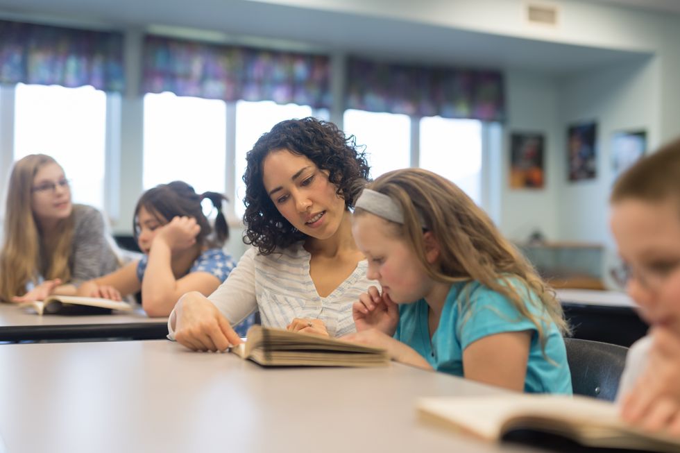 Elementary teacher helping a student at her desk Lehrerin betreut lesende Schülerin.