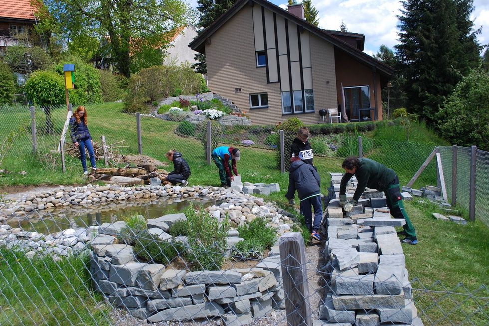 Kinder bauen draussen an Mauern und einem Weiher.