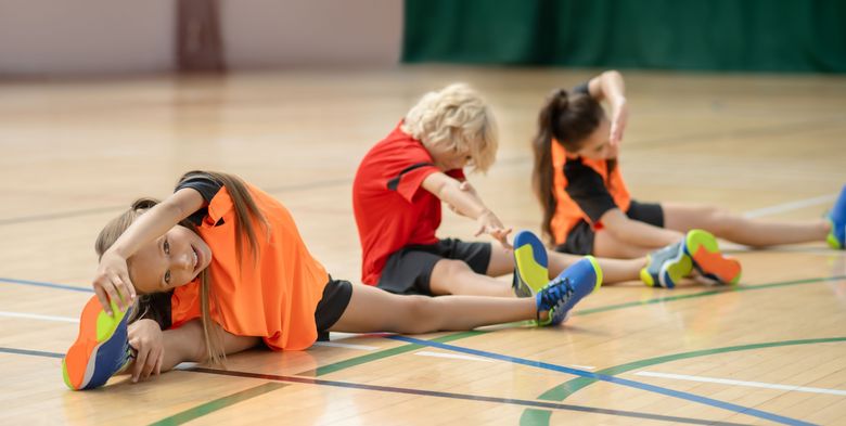 Three kids sitting on the floor and stretching Kinder dehnen in einer Turnhalle Beine und Arme