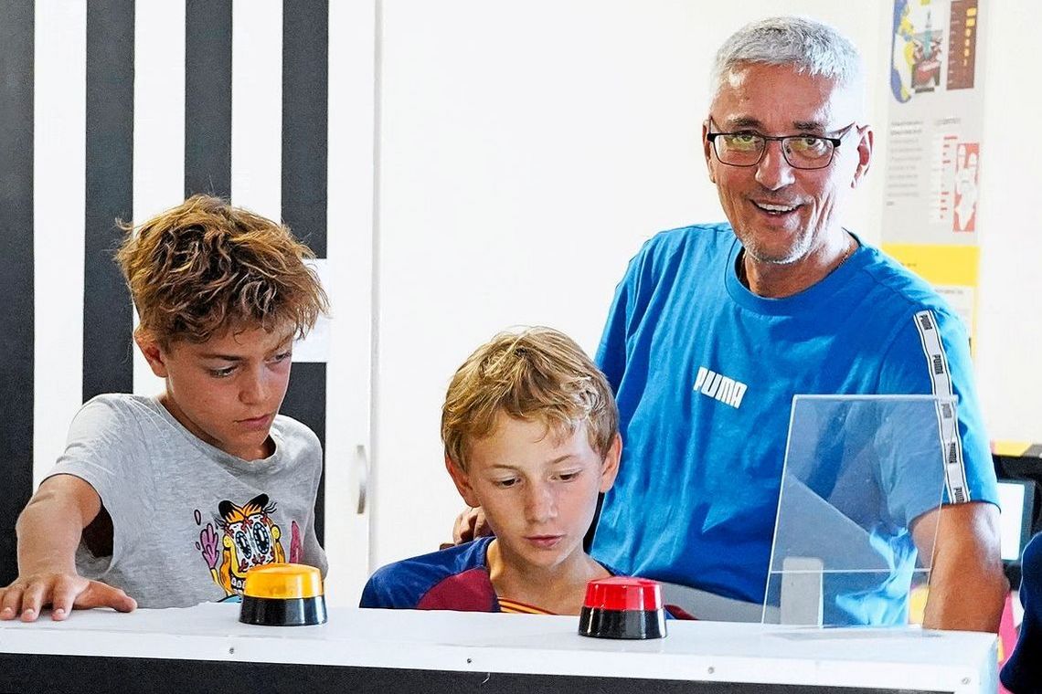 Ein Erwachsener Mann und zwei Kinder stehen vor einer Maschine, auf der sich zwei Warnlichter befinden.