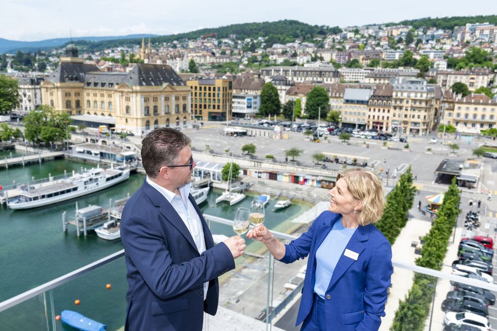 David Rey und Dagmar Rösler stossen auf einer Dachterrasse zusammen an. Im Hintergrund ist die Stadt Neuenburg.
