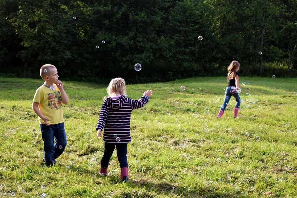 Drei Kinder spielen auf einer Wiese mit Seifenblasen.