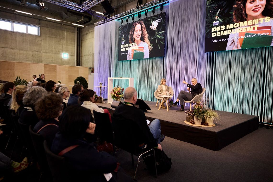 Menschen auf Stühlen sitzen zwei Personen, die auf einer Bühne sitzen, gegenüber.
