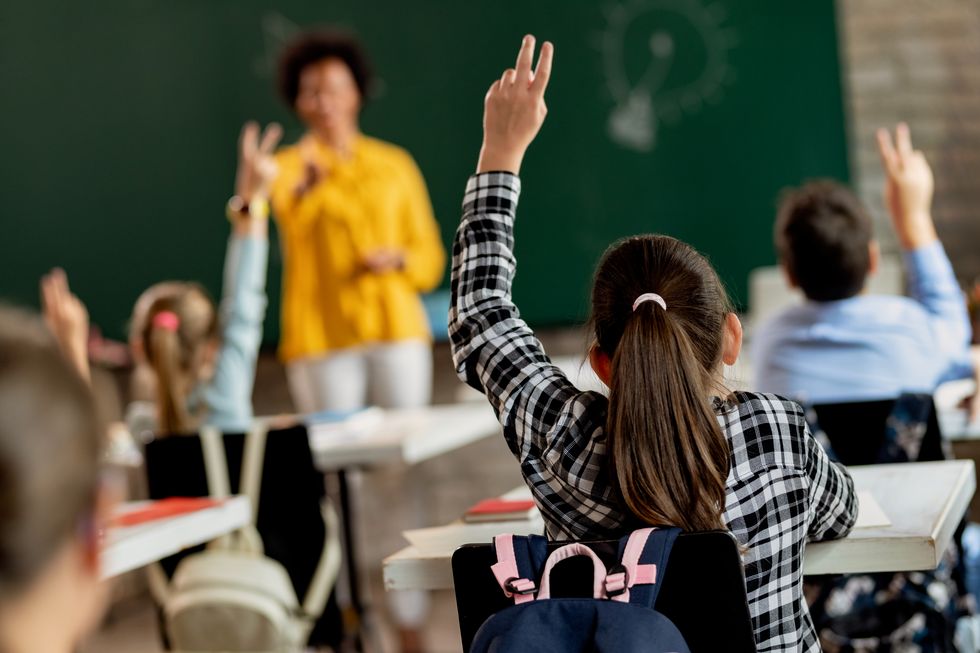 Schülerin im Klassenzimmer, die im Unterricht den Arm hebt, um sich zu melden.