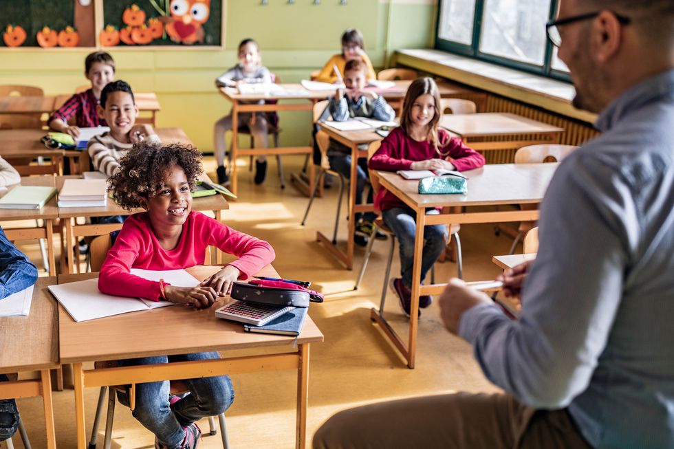 Large group of happy students listening to their elementary teacher at school. Lehrer unterrichtet Primarschüler.
