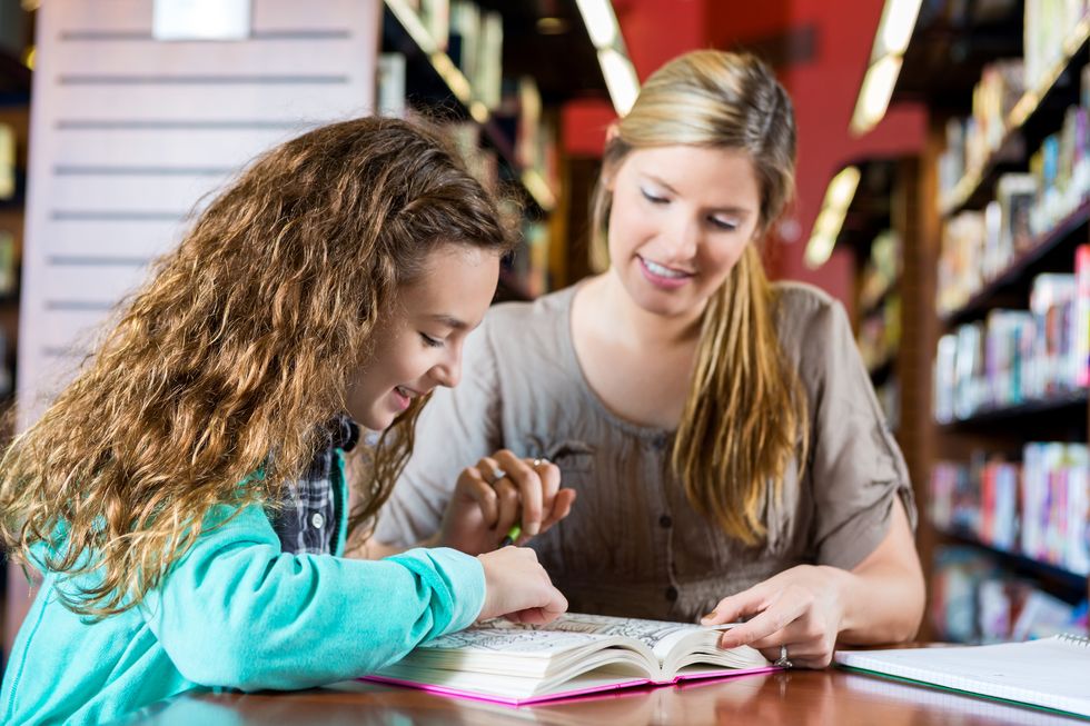 Eine Frau und ein Kind lesen zusammen in der Bibliothek ein Buch.