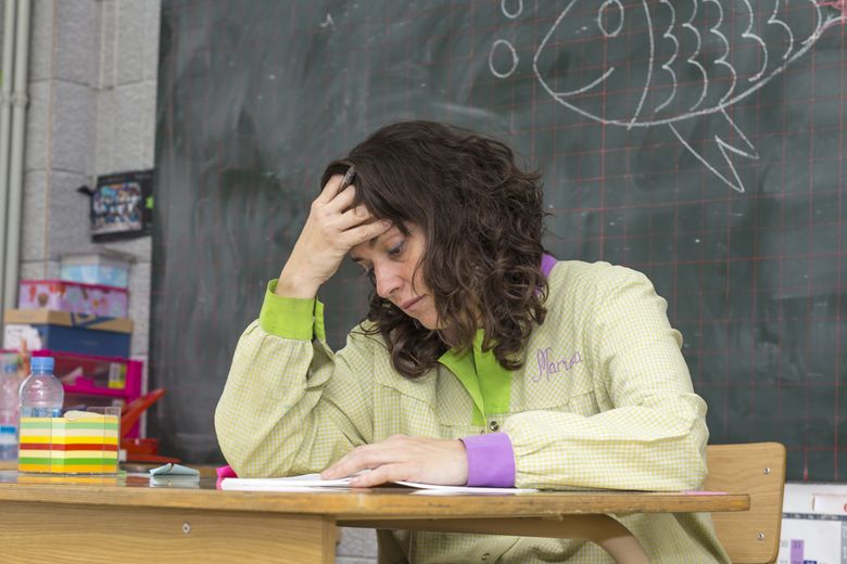 Lehrerin sitzt am Pult und stützt sich den Kopf.