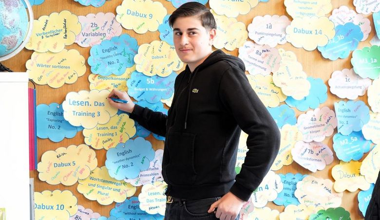 Junge steht vor einer Wand, die mit Wolken aus Papier.