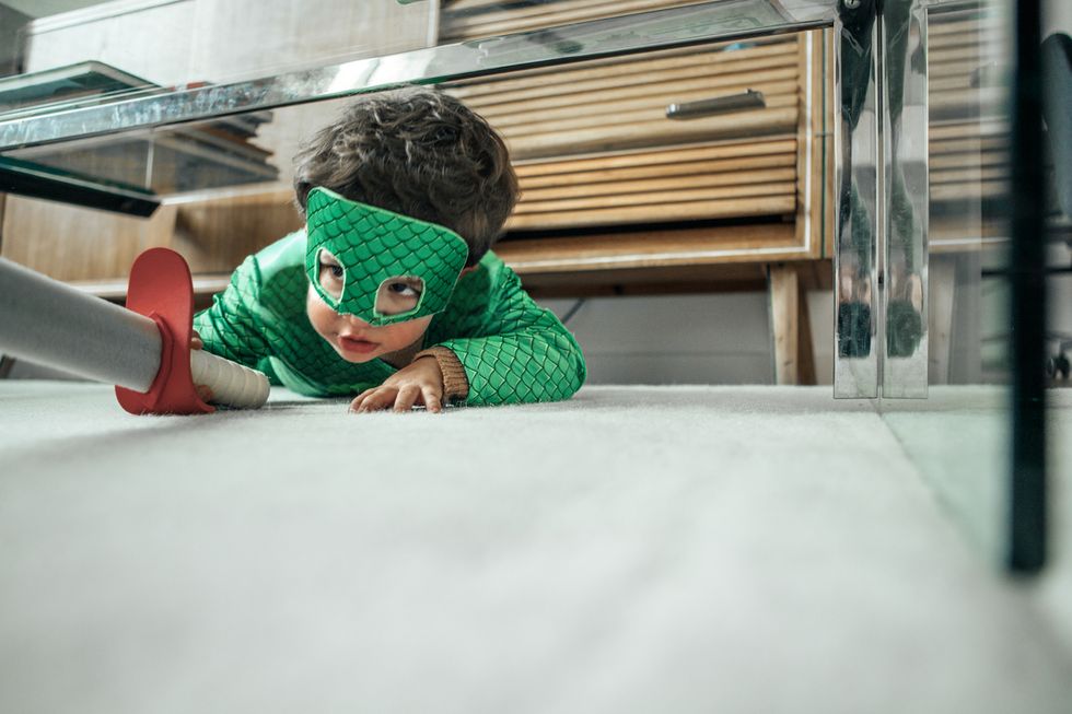 Kind krabbelt als Ritter verkleidet mit Spielzeugschwert unter einen Tisch.