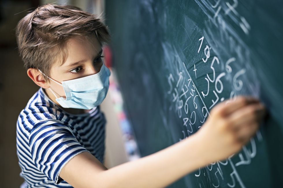 Präsenzunterricht mit Hygienekonzept: Schüler mit Gesichtsmaske löst an der Tafel eine Matheaufgabe.