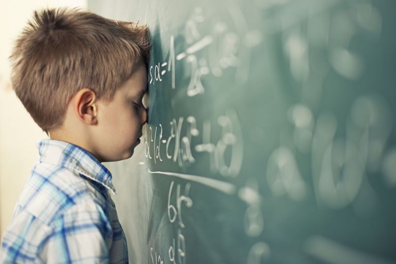 Ein Kind lehnt mit der Stirn an eine Wandtafel, auf der mehrere mathematische Formeln stehen.
