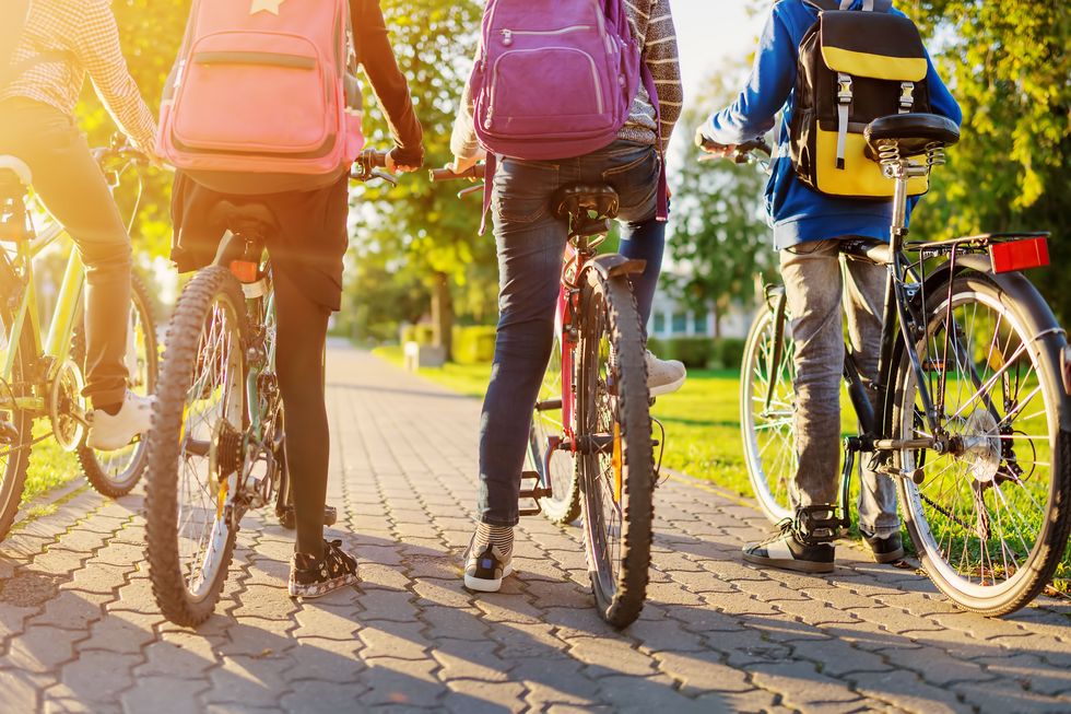 Children with rucksacks riding on bikes in the park near school