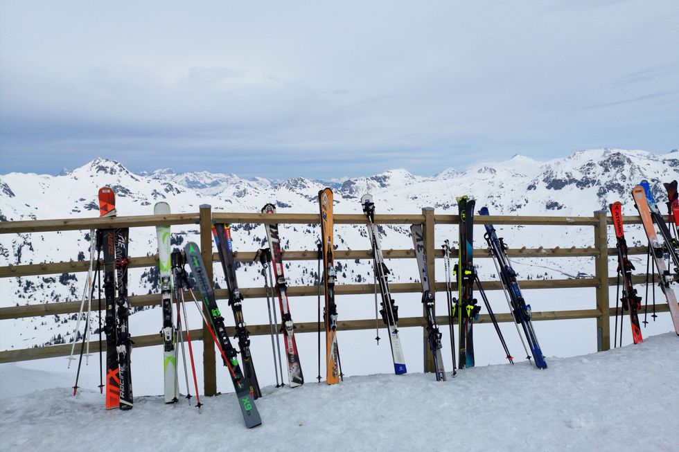 Skis und Stöcke lehnen an einem Holzzaun vor einem Bergpanorama.