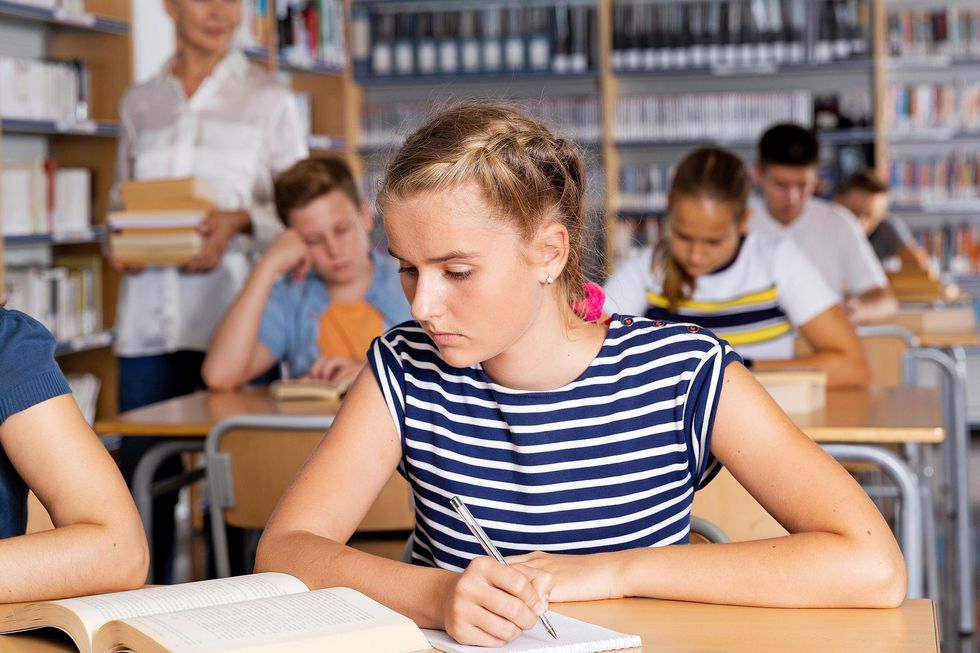 1312439246 Mädchen sitzt im Unterricht und macht Notizen.