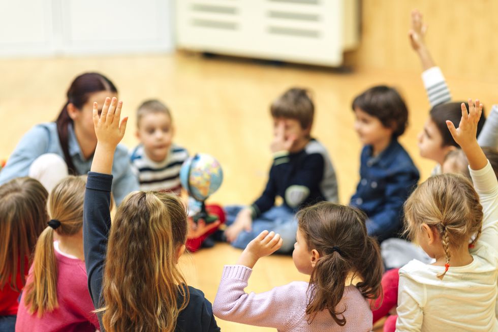 Lehrerin sitzt mit Kindern in einem Kreis.