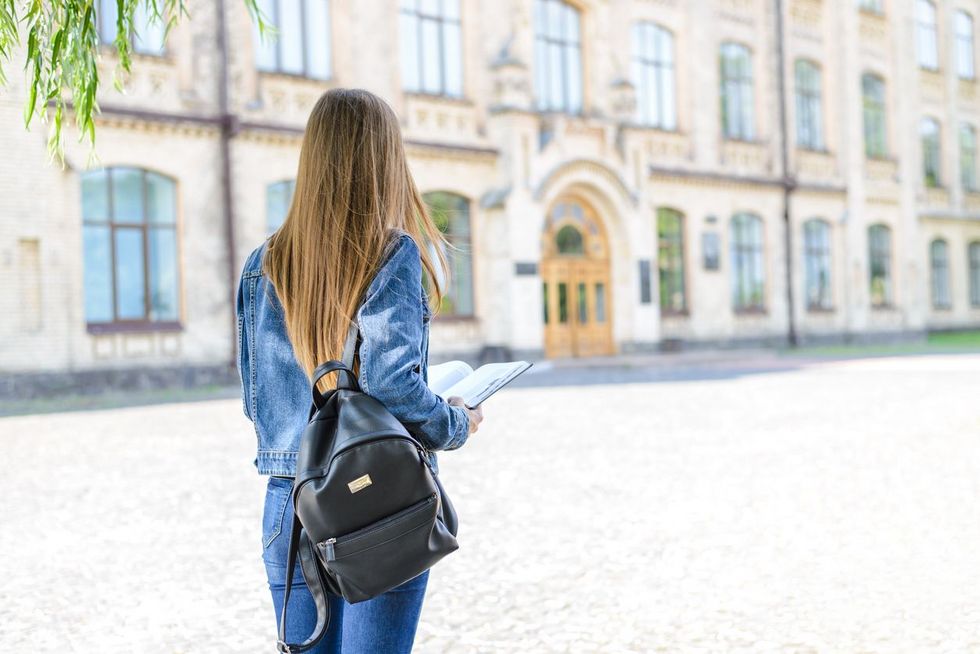 Junge Frau mit Rucksack steht in einiger Entfernung zu einem Gebäude mit geschlossener Tür.