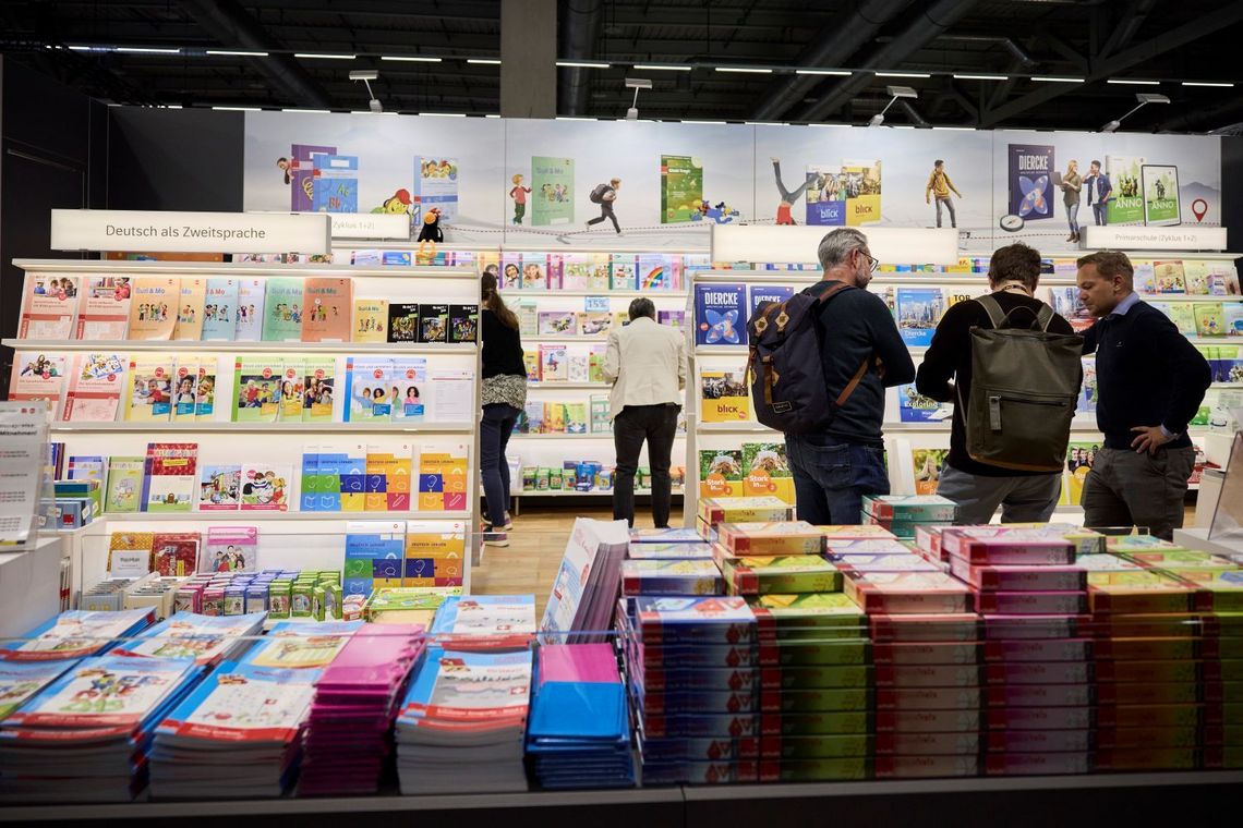 Drei Personen schauen sich vor einer Bücherauslage ein Lehrmittel an