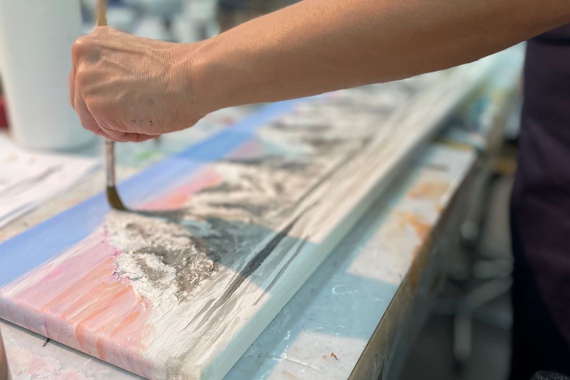 eine Frau malt mit einem Pinsel eine Berglandschaft