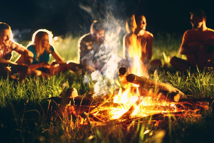 Eine Gruppe junger Menschen sitzt im Kreis um ein Lagerfeuer