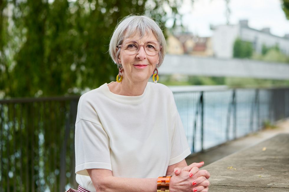 Frau mit beigem Oberteil sitzt an einem Tisch an einem Flussufer.