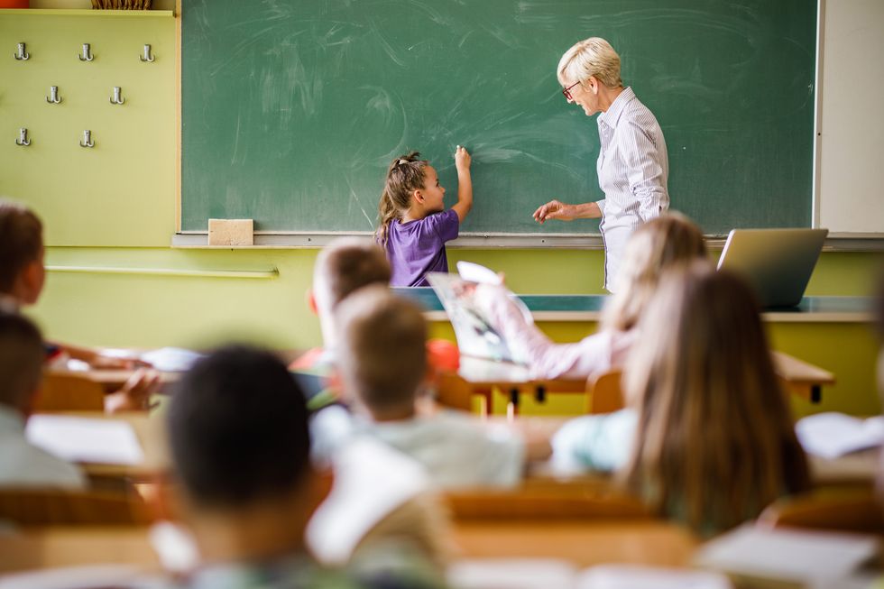 Ein Mädchen steht zusammen mit einer Lehrerin vor der Tafel.