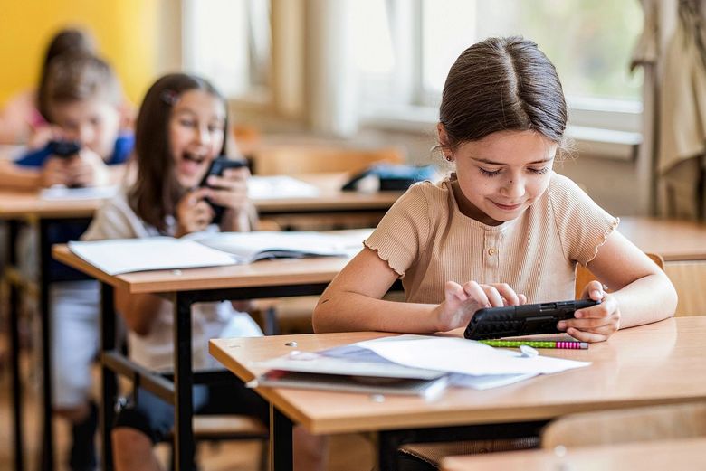 Kinder sitzen an Schulbänken und benutzen ihre Smartphones.