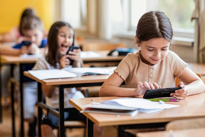 Kinder sitzen an Schulbänken und benutzen ihre Smartphones.